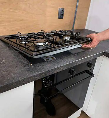 A person's hand carefully positioning a gas cooktop into a granite countertop in a modern kitchen setting.