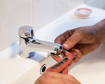 Close-up of a plumber's hands using an adjustable wrench to repair a shiny chrome bathroom sink faucet.