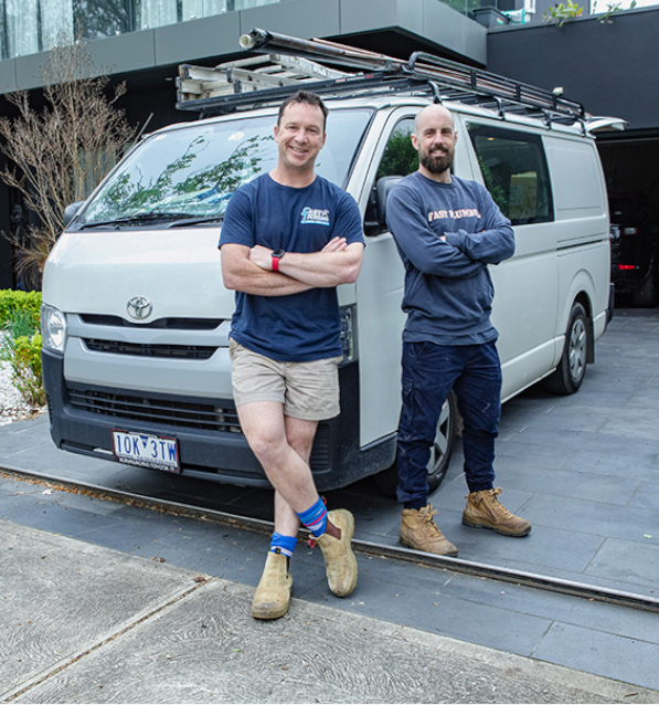 Friendly Melbourne plumber duo standing in front of their plumbing van