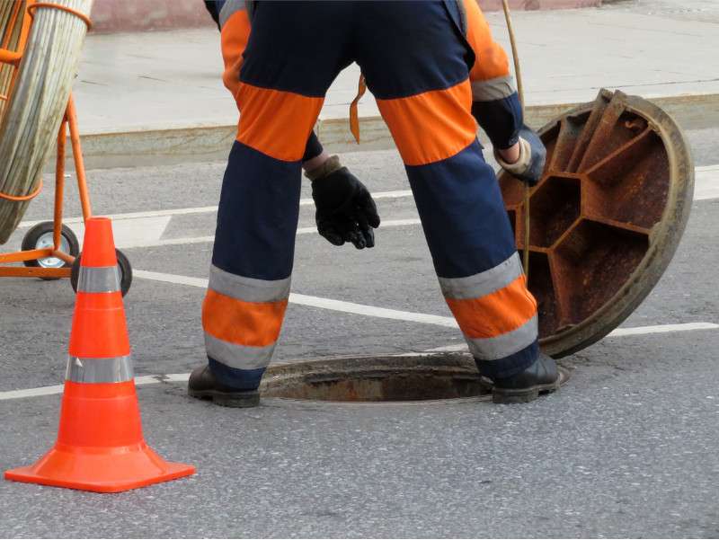 Worker in uniform stand over the open sewer hatch.