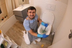 A man in his forties wearing an apron is using a plunger in the bathroom. He is trying to solve a toilet blockage