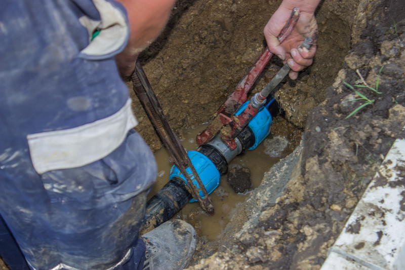 Utility workers holds wrench and in trench repair the broken pipe for irrigation system.