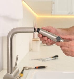 Plumber repairing water tap in kitchen, closeup.