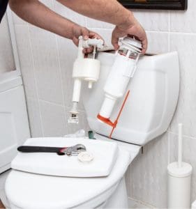 Man using tools repairing reservoir in a bathroom in a concept of DIY repairs with copy space.